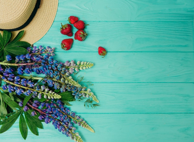 Летняя концепция, соломенная шляпа, свежая клубника и цветы на деревянном фоне