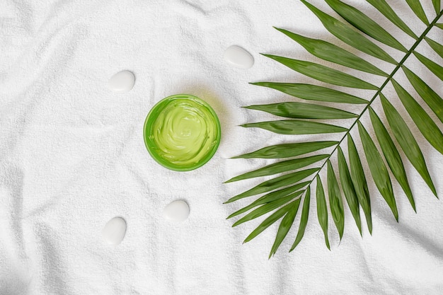 Summer cosmetics moisturizing gel green color and palm leaf on the towel and white stones background for spa