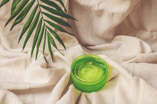 Фото Летняя косметика увлажняющий гель зеленого цвета с пальмовым листом на фоне льняной ткани