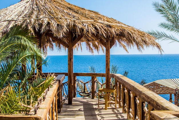 Cottage estivo con tetto di paglia sulla riva del mare blu sullo sfondo del cielo azzurro tra le palme verdi