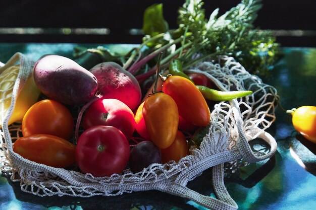 Estate raccolto verdure pomodori colorati barbabietola in eco borsa a rete sotto le ombre dure alla moda