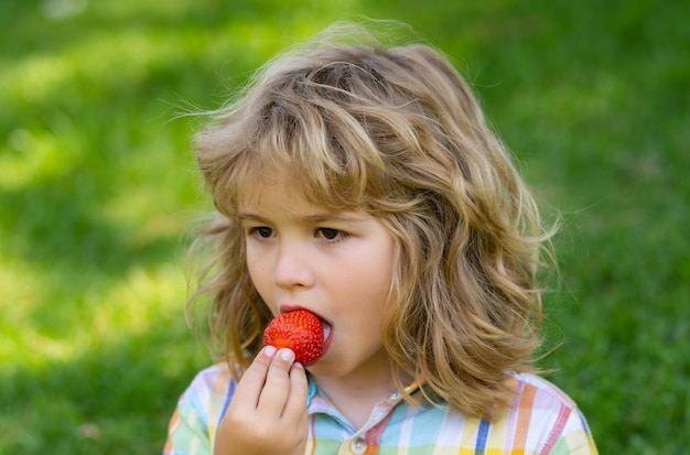 Foto l'estate faccia bambino carino da vicino bambini faccia con fragola in bocca bambino mangiare bacche di fragola nel