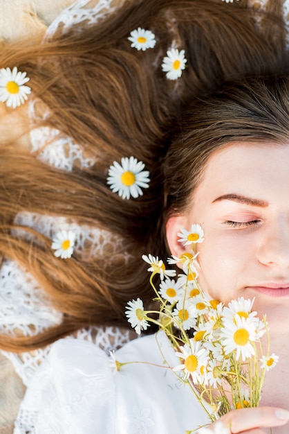 Summer day, picnic in the village. A beautiful girl in a hat lies on a plaid plaid. a bouquet of daisies, flowers in her hair.