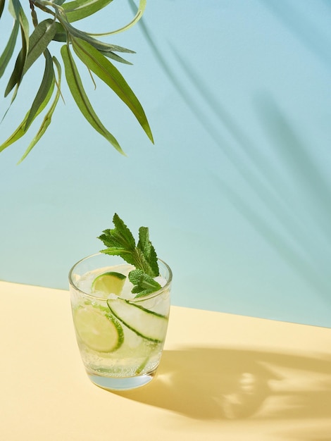 Summer drink in crystal glass with lime cucumber and mint on yellow and blue background with leaves