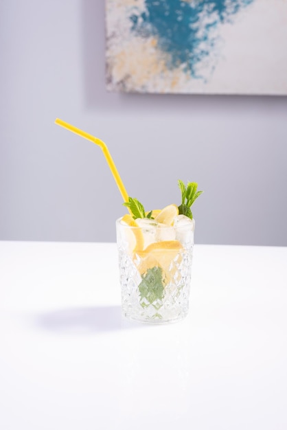 Летний напиток в стеклянном стакане с лимонной мятой и льдом на белом столе Минимальная летняя освежающая концепция