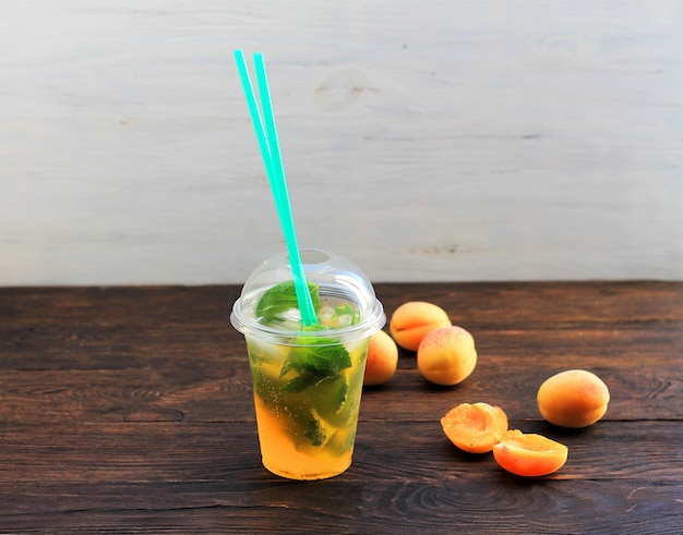 Estate bere limonata con arancia e menta nella tazza di plastica su uno sfondo scuro.