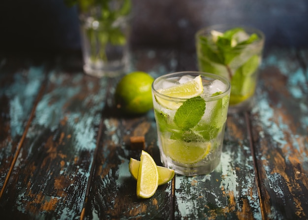 Summer drink Mojito with ice, brown sugar, lime slices, fresh mint in glass, wooden rustic background, angle view. Cold refreshing cocktail great for summer party and fun