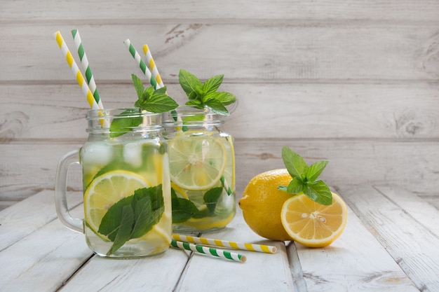 Summer drink with lemon, ice and mint in mason jar on a white wooden background.