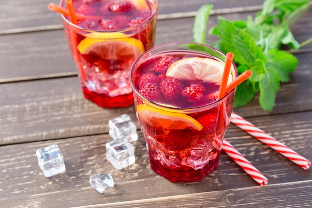 Photo summer drink with raspberries, lime and ice on a old wooden table