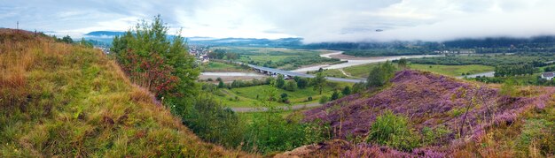 Summer evening country foothills panorama with heather flowers and wooden cross (Lviv Oblast, Ukraine) . Three shots stitch image.