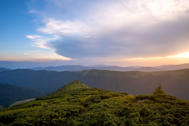 Summer evening mountain landscape with grassy hills and distant peaks at colorful sunset.