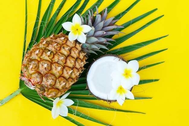 Summer f top view scene with fresh tropical green leaves coco and pineapples close up on yellow background