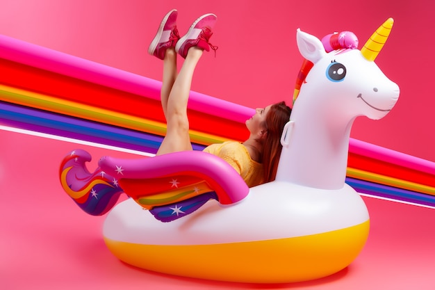 Summer fashionable girl, pink and joyful mood. Beautiful slim woman in a summer clothes, having fun and enjoying life on a white inflatable unicorn