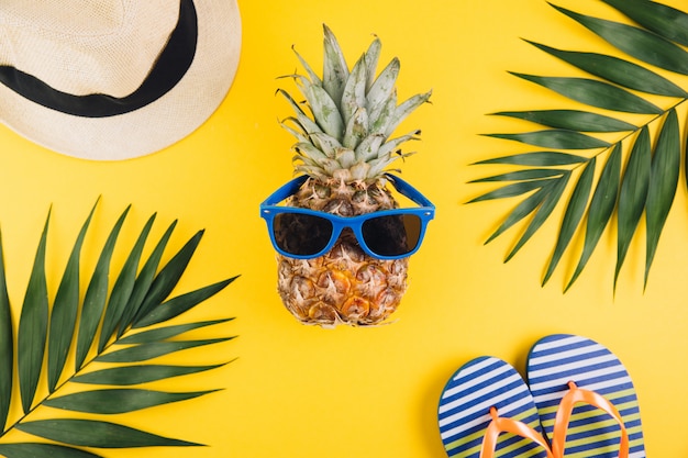 Summer flat lay background. Palm leaves, flip flops, pineapple, sunglasses and straw hat on yellow background.