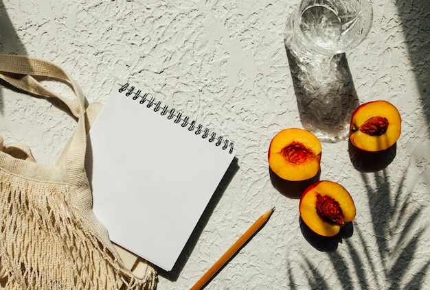 Summer flat lay on a concrete background Notepad peaches and an ecofriendly mesh shopping bag