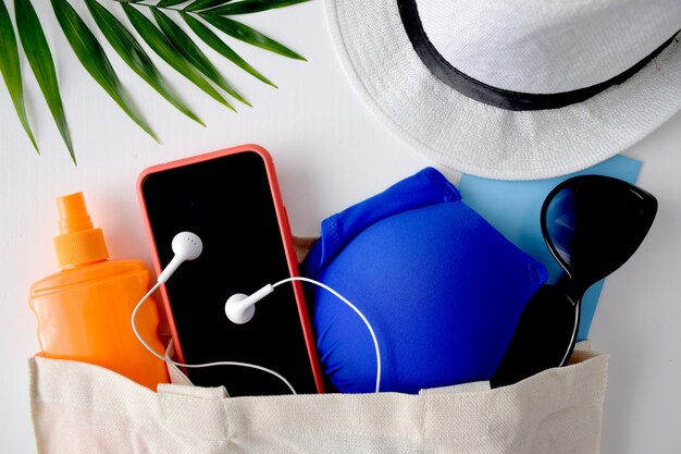 Summer flat lay traveller accessories, palm leaf, hat, sunglasses, phone, sunscreen, headphones