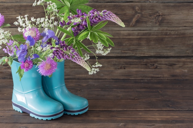 Summer flowers in rubber boots on old dark wooden background