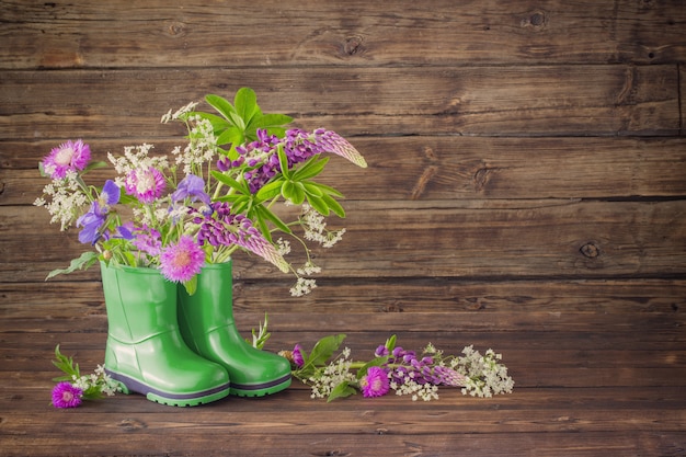 Summer flowers in rubber boots on old dark wooden