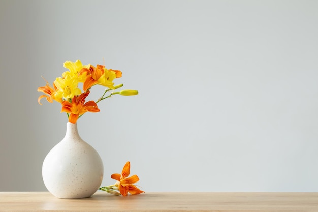 Летние цветы в белой современной вазе на деревянной полке