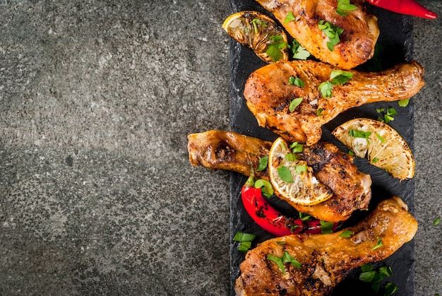 Summer food Ideas for barbecue grill party Chicken legs wings grilled fried on fire With hot chili pepper lemon and bbq sauce Dark stone table 