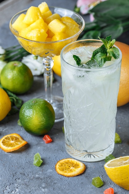 Summer fresh cold drink beverages. Ice Lemonade in the jug and lemons and orange with mint on the table outdoor. Orange lemonade in a glass