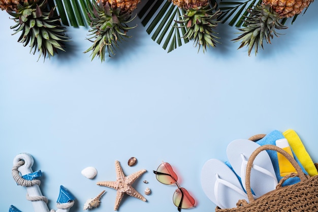 Concetto di design di sfondo di frutta estiva vista dall'alto della spiaggia da viaggio con conchiglie, cappello di ananas e foglie di palma su sfondo blu