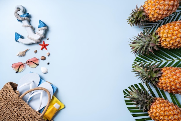 Summer fruit background design concept Top view of holiday travel beach with shells hat pineapple and palm leaves on blue background