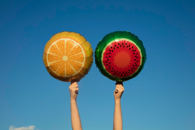 Summer fruit balloons held in the air against a bright blue summer sky