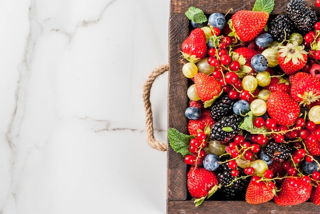 Summer fruit and berries.  types of raw organic farmer berries  raspberries blackberries blueberries strawberries red currants gooseberries. White marble table, wooden tray box.  top view