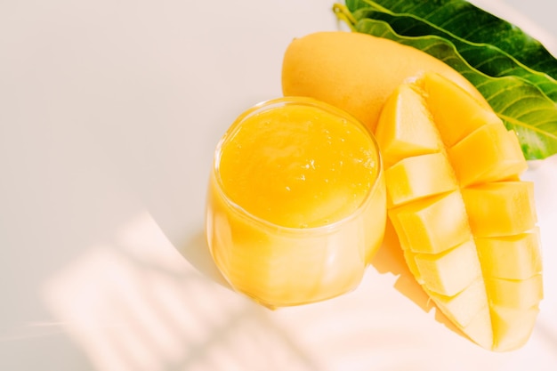 Foto frutta estiva a fetta e succo di mango con ombra di foglia tropicale e sfondo bianco