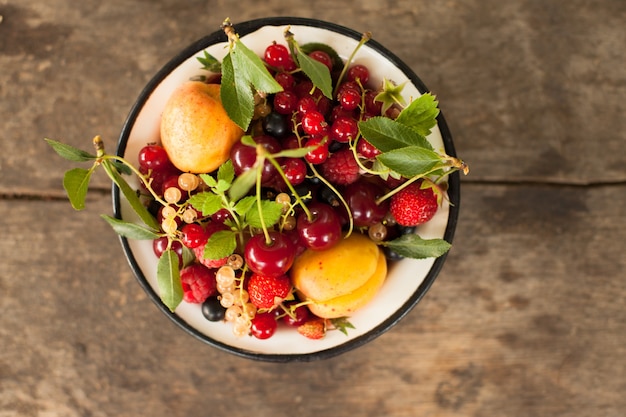 Summer fruits in enamelled metal bowl on wooden table