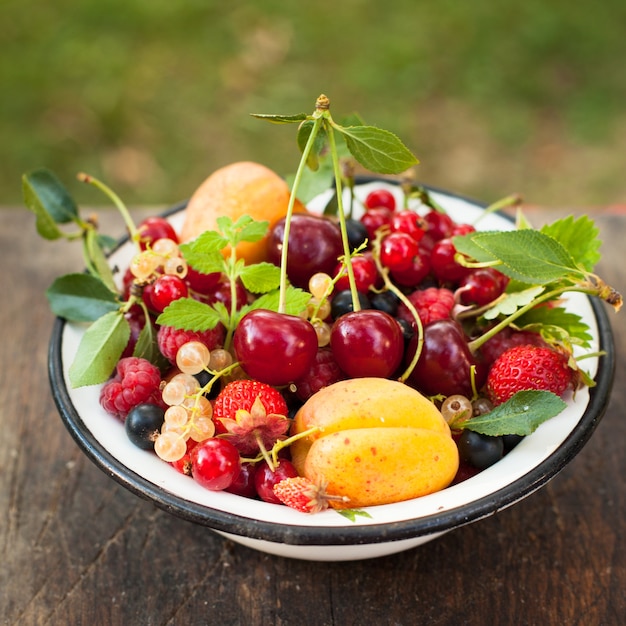 Summer fruits in enamelled metal bowl on wooden table