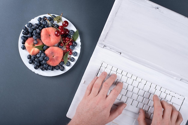 흰색 페인트 복숭아와 체리로 된 노트북이 있는 회색 배경의 여름 과일