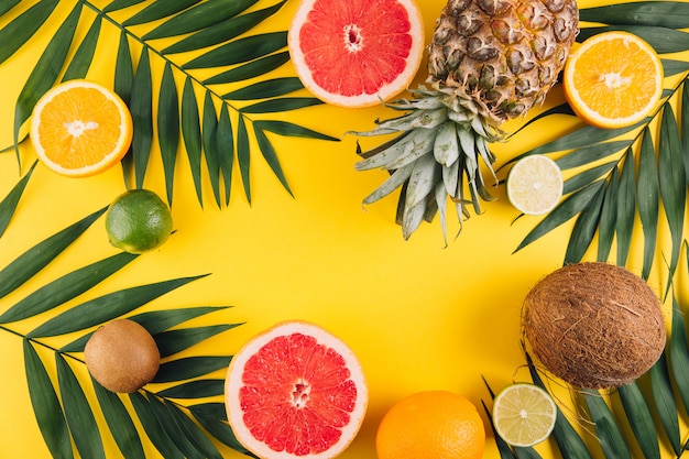 Summer fruits. Tropical palm leaves, pineapple, coconut, grapefruit, orange and lime on yellow background. 