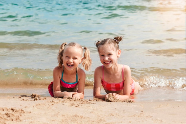 Летние развлечения на морском пляже Счастливые дети Сестры лежат весело смеются на песке на фоне моря