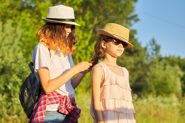 Foto estate, bambini felici che camminano godendosi le vacanze nella natura, la sorella maggiore intreccia i suoi capelli più giovani.