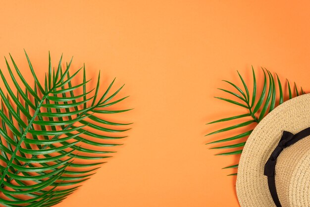 Summer hat lay on green leaf on orange background. Copy space.