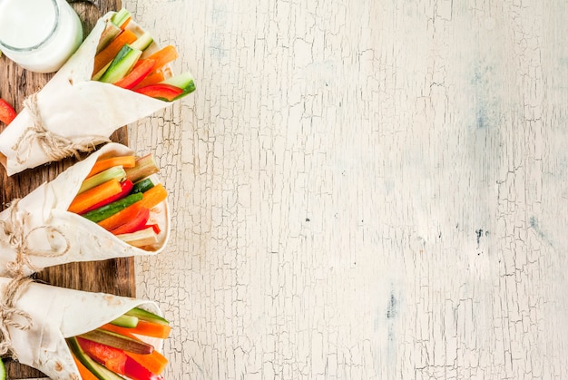 Summer healthy snack appetizer, Mexican style tortilla sandwich wraps assorted colorful fresh vegetable sticks (celery, rhubarb, pepper, cucumber and carrot) with yoghurt sauce dip above