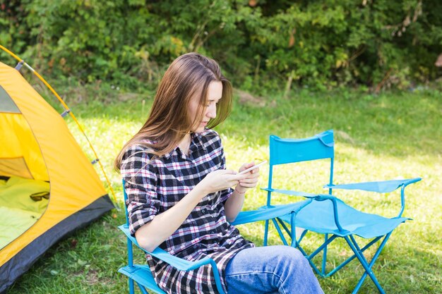 Summer, hike, tourism and nature concept - young woman sitting near tent