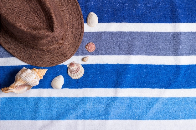 A summer holiday composition on a beach towel with seashells and a hat.