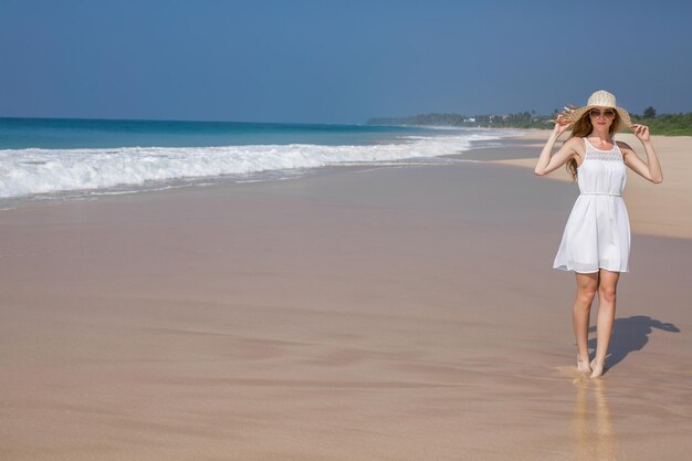 Summer holiday fashion concept tanning woman wearing sun hat at the beach on a white sand shot from above