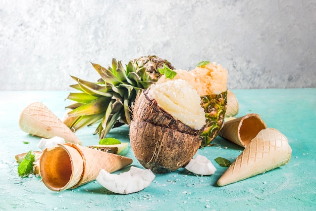 Summer holiday vacation concept, set various tropical ice cream sorbets, frozen juices in pineapple, grapefruit and coconut, light blue concrete 