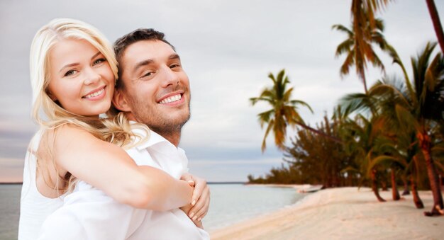 summer holiday, vacation, dating, travel and tourism concept - happy couple having fun and hugging over beach background