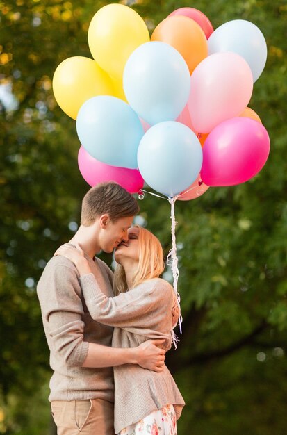 летние каникулы, праздник и концепция свиданий - пара с разноцветными воздушными шарами целуется в парке