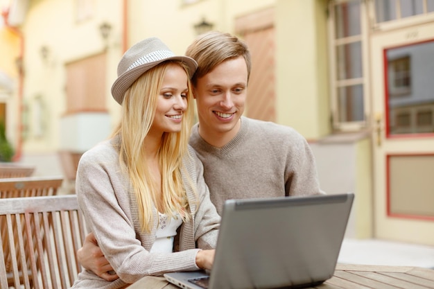 summer holidays, city, dating and technology concept - smiling couple with laptop computer in cafe