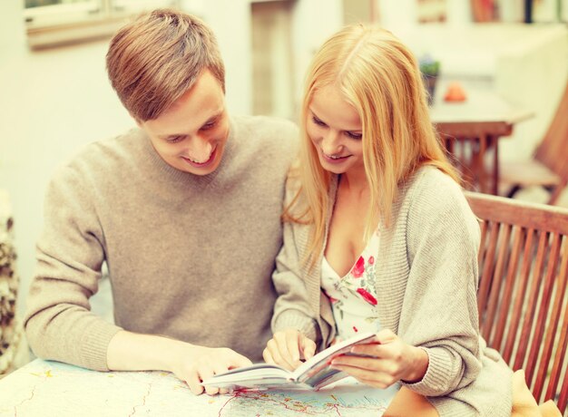 summer holidays, dating, city break and tourism concept - happy couple with map, camera and travellers guide in cafe