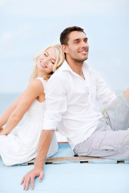 summer holidays and dating concept - couple in shades sitting at sea side