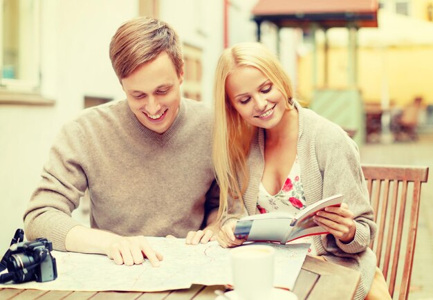 summer holidays, dating and tourism concept - couple with map, camera, travellers guide and coffee in cafe