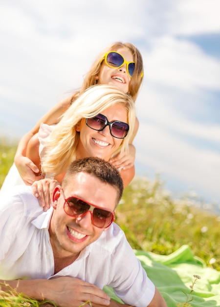 summer holidays, family, child and happy people concept - smiling family in sunglasses lying on blanket outdoors