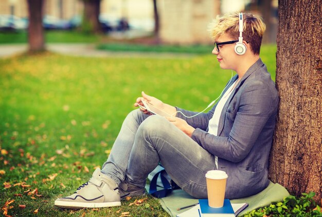 summer holidays, internet and technology concept - teenager with headphones, books, coffee and tablet pc outside